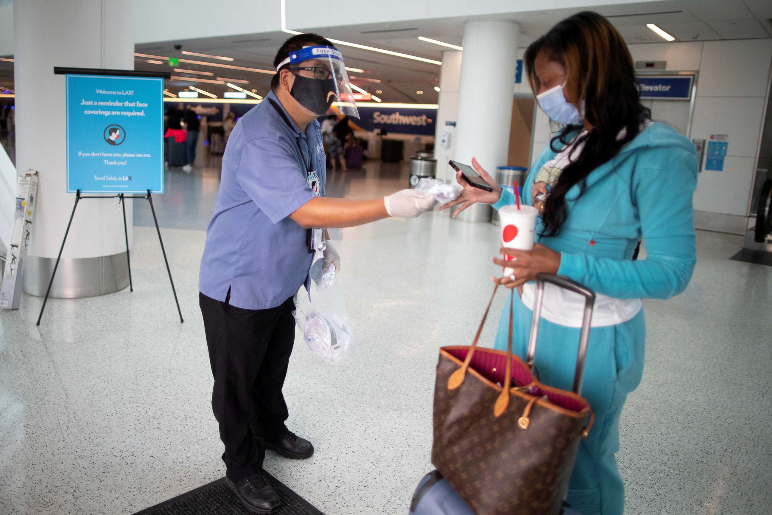 PHOTO: Travel Safely Ambassador Carlos Hernandez hands out a face masks to an airline passenger at LAX airport, as the global outbreak of the coronavirus disease (COVID-19) continues, in Los Angeles, Aug. 4, 2020.