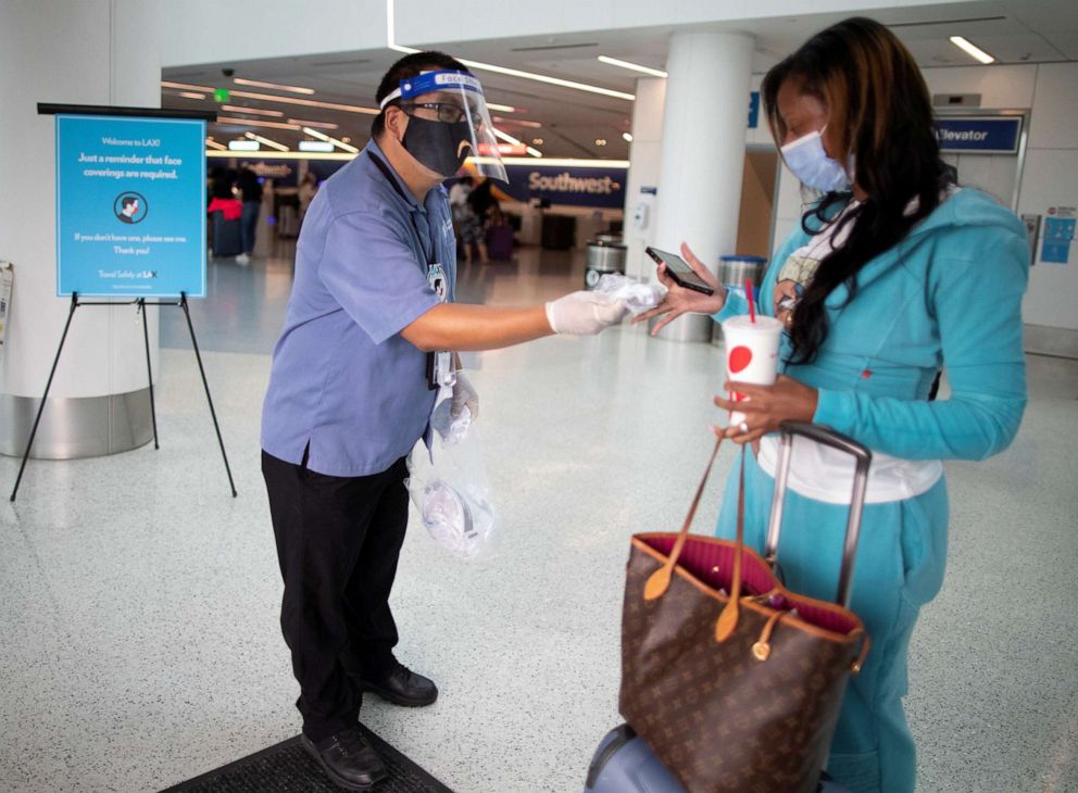 PHOTO: Travel Safely Ambassador Carlos Hernandez hands out a face masks to an airline passenger at LAX airport, as the global outbreak of the coronavirus disease (COVID-19) continues, in Los Angeles, Aug. 4, 2020.