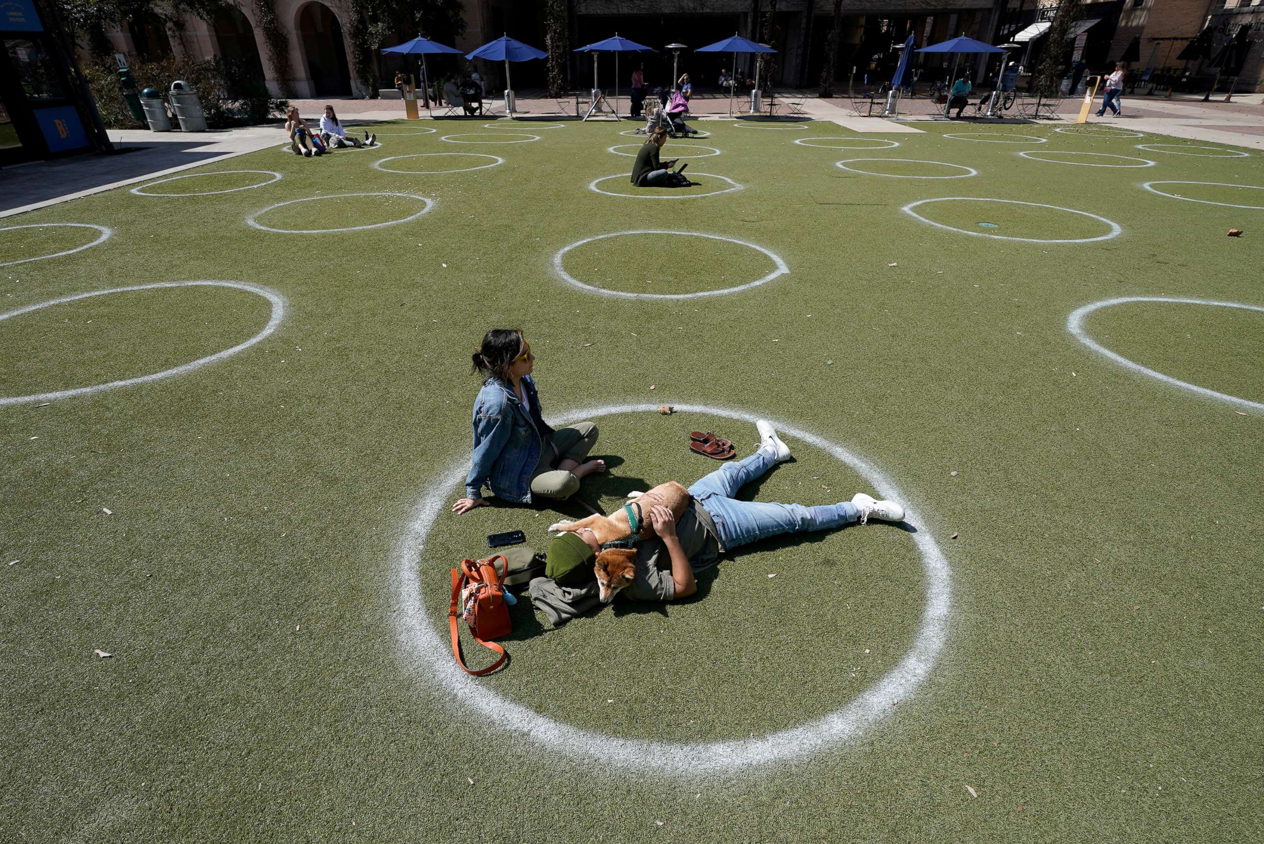 PHOTO: Kyree Kayoshi, his dog Kumi, and Miranda De Llano use circles marked for social distancing to help battle the COVID-19 virus as they relax at the Pearl Brewery, March 3, 2021, in San Antonio, Texas. 
