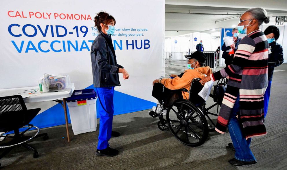 PHOTO: Everlean Jackson, 75, pushes her husband Elton in his wheelchair on arrival for their COVID-19 vaccine to be administered by Kathryne Acuna (L), Director of Ambulatory Clinical Services at Kaiser Permanente in Pomona, Calif., Feb. 5, 2021. 