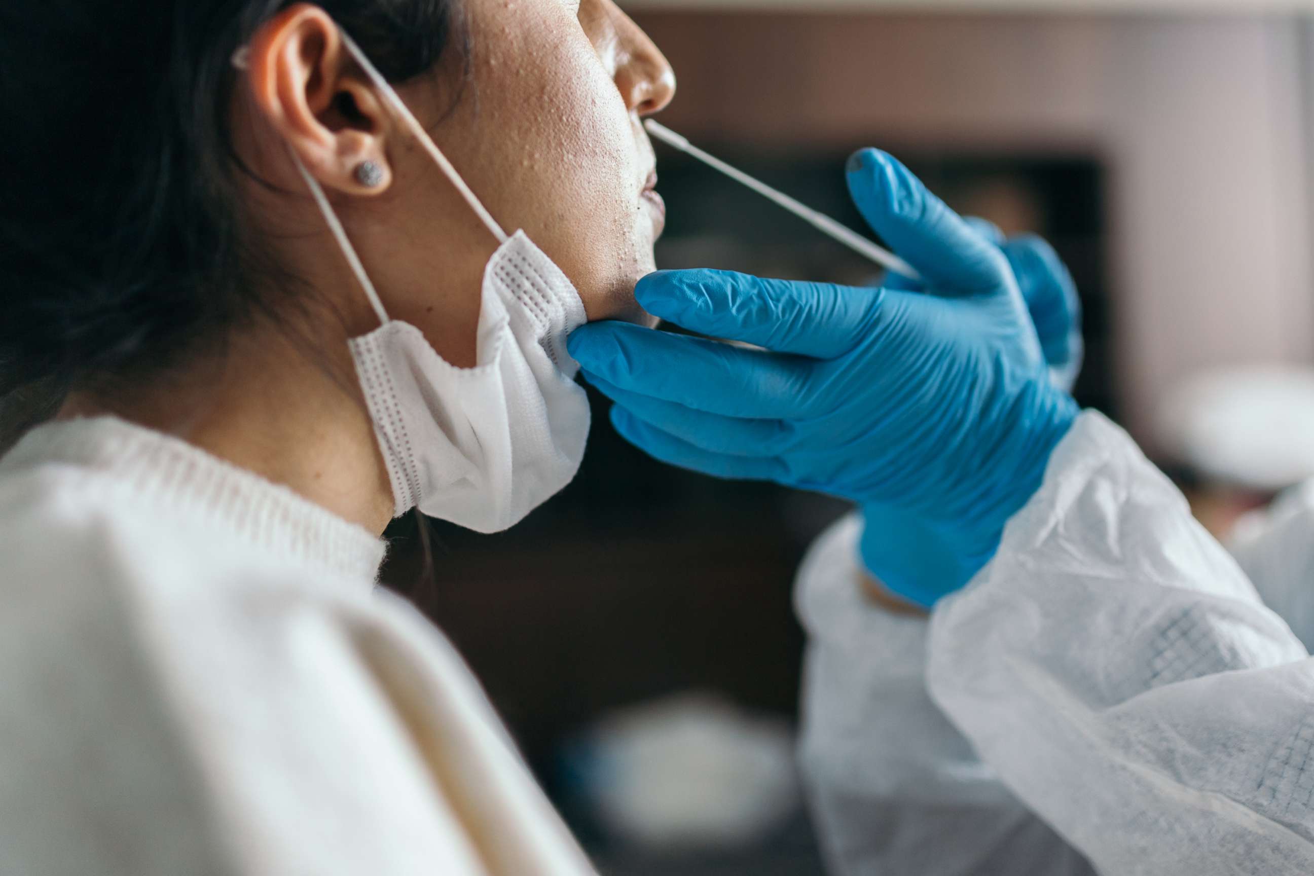 PHOTO: Doctor in protective workwear taking nose swab test from young woman