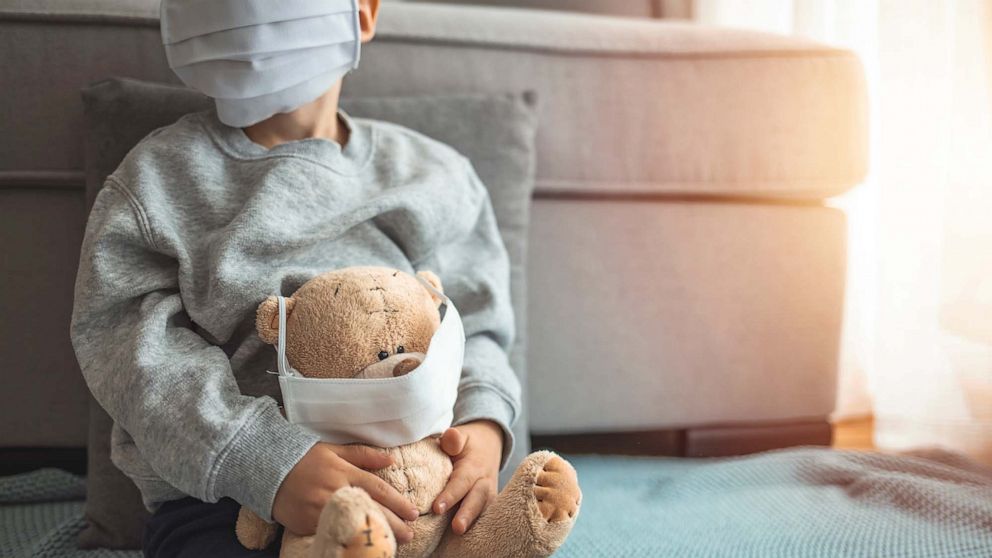 PHOTO: A child wearing a covid-19 protective mask holds a masked teddy bear in an undated stock image.