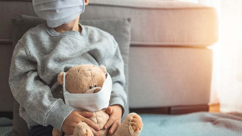 PHOTO: A child wearing a covid-19 protective mask holds a masked teddy bear in an undated stock image.