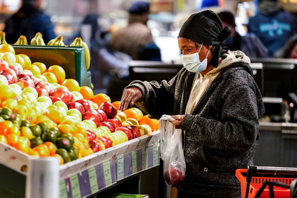PHOTO: A shopper waring a protective mask as a precaution against the spread of the coronavirus selects fruit at the Reading Terminal Market in Philadelphia, Feb. 16, 2022.