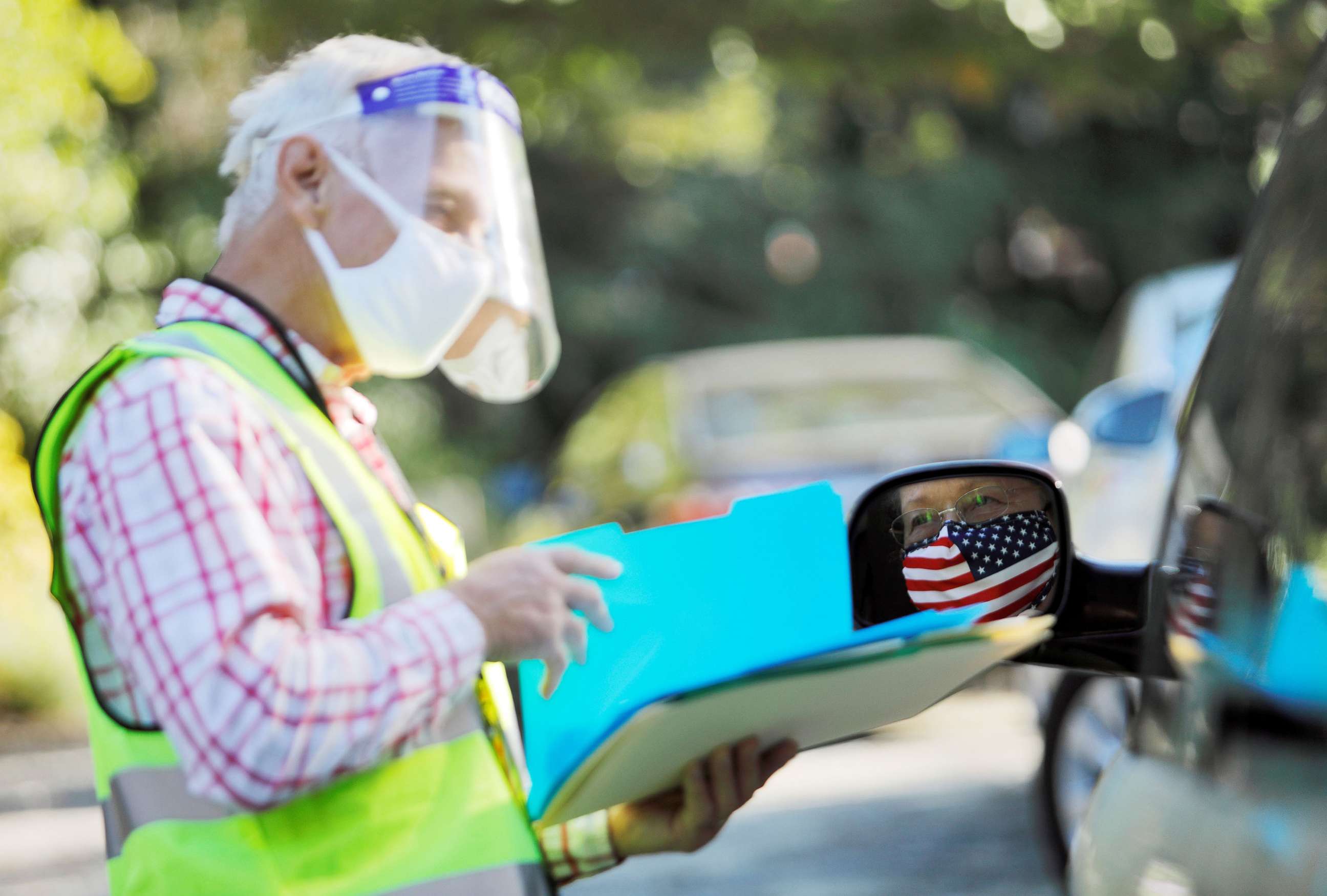 PHOTO: An election worker wearing a mask and face shield for COVID-19 assists a voter casting her ballot from her car on the first day of the state's in-person early voting for the national elections in Durham, N.C., OCT. 15, 2020.