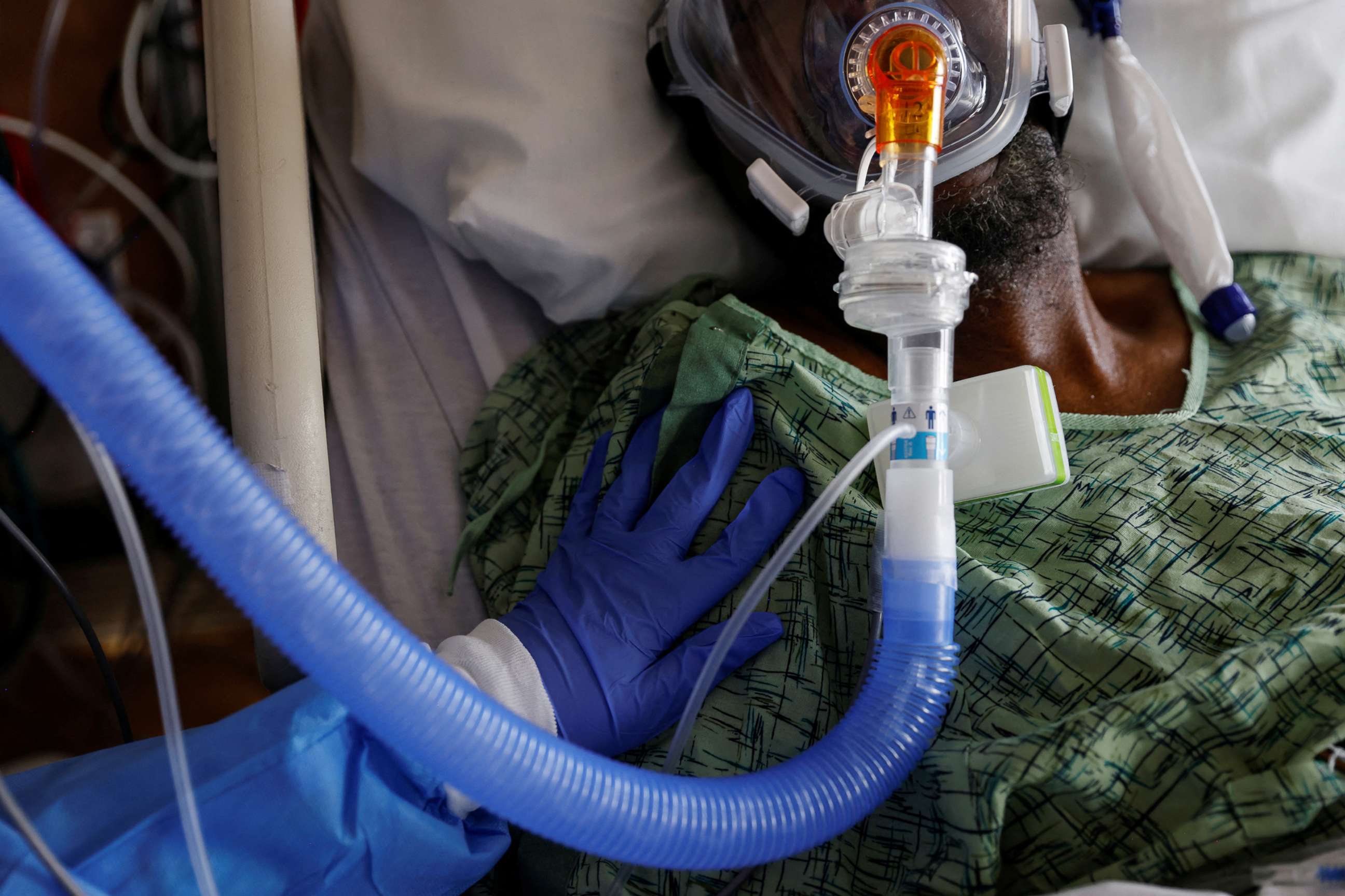 PHOTO: Sandie Bushnur, a hospital sitter who provides companionship, observation, and surveillance, places her hand on a COVID-19 patient in the Intensive Care Unit (ICU) at St. Mary Medical Center in Apple Valley Calif.,  Feb. 1, 2022. 