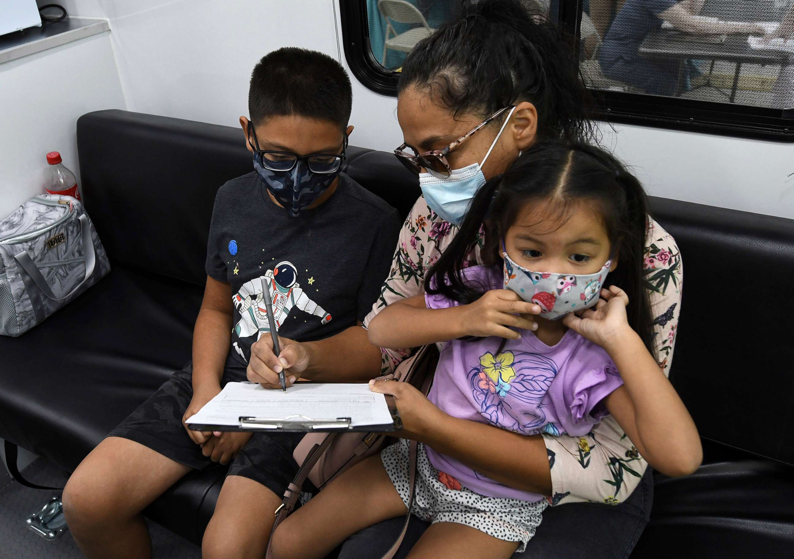 PHOTO: A boy waits while his mother signs a form required for him to receive a shot of the Pfizer COVID-19 vaccine at a mobile vaccination site on May 22, 2021, in Orlando, Fla.