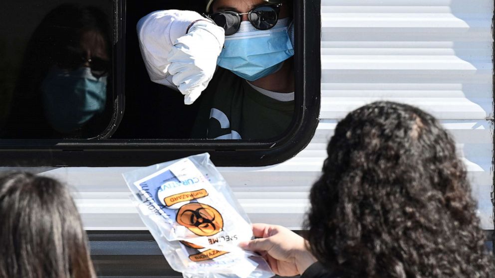 PHOTO: A CORE (Community Organized Relief Effort) worker hands COVID-19 test kits to people at a walk-up testing site in south Los Angeles, California, on Dec. 1, 2020.