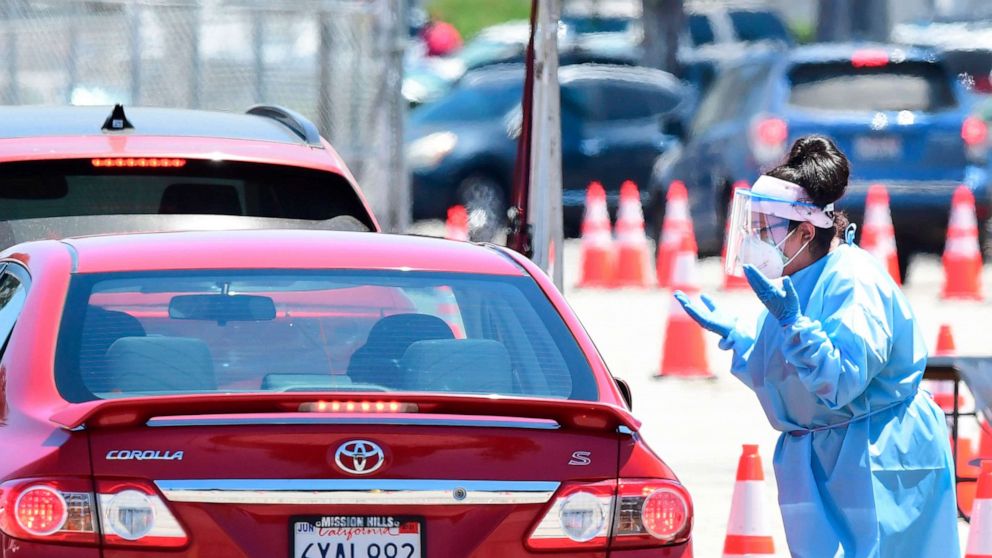 PHOTO: A volunteer dressed in personal protective equipment gestures to a driver in line at a COVID-19 testing site in the Panoramic City neighborhood of Los Angeles, California, on July 30, 2020.