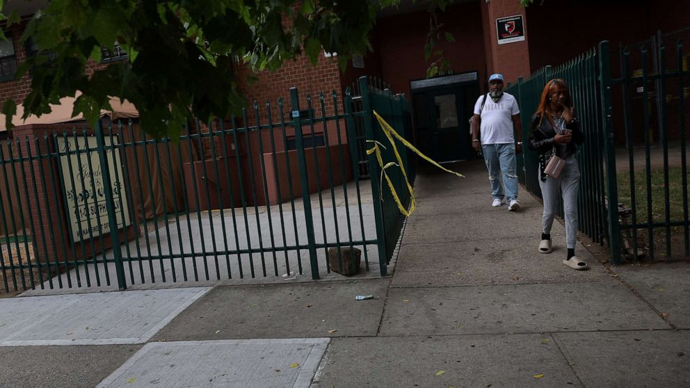 PHOTO: People walk by NYPD police tape and a blood stained sidewalk, where according to police reports a shooting killed one man and injured another Wednesday night outside an apartment building in the South Jamaica section of Queens, July 7, 2022.