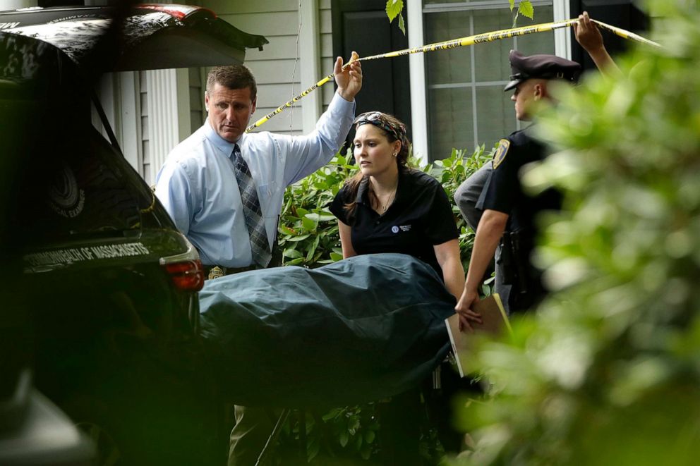 PHOTO: A woman from the Massachusetts Chief Medical Examiners Office, center, uses a gurney to place human remains into a vehicle at a home where two adults and three children were found dead with gunshot wounds, Oct. 7, 2019, in Abington, Mass.