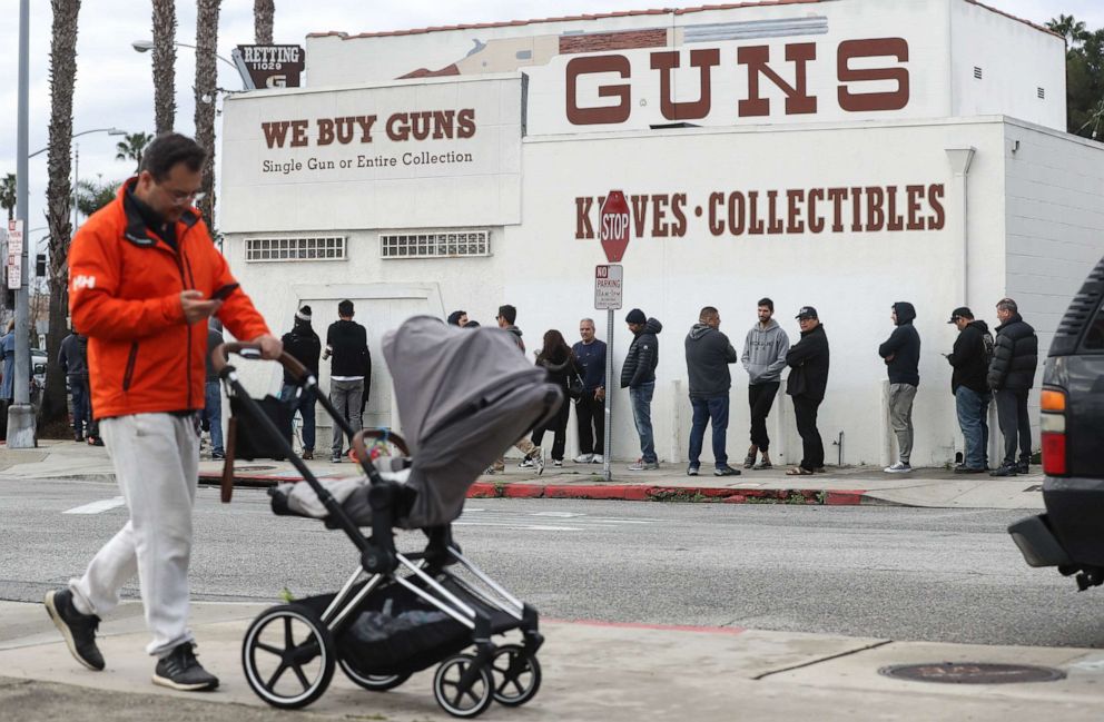 PHOTO: A man walks with a stroller as people stand in line outside the Martin B. Retting, Inc. gun store on March 15, 2020, in Culver City, Calif.