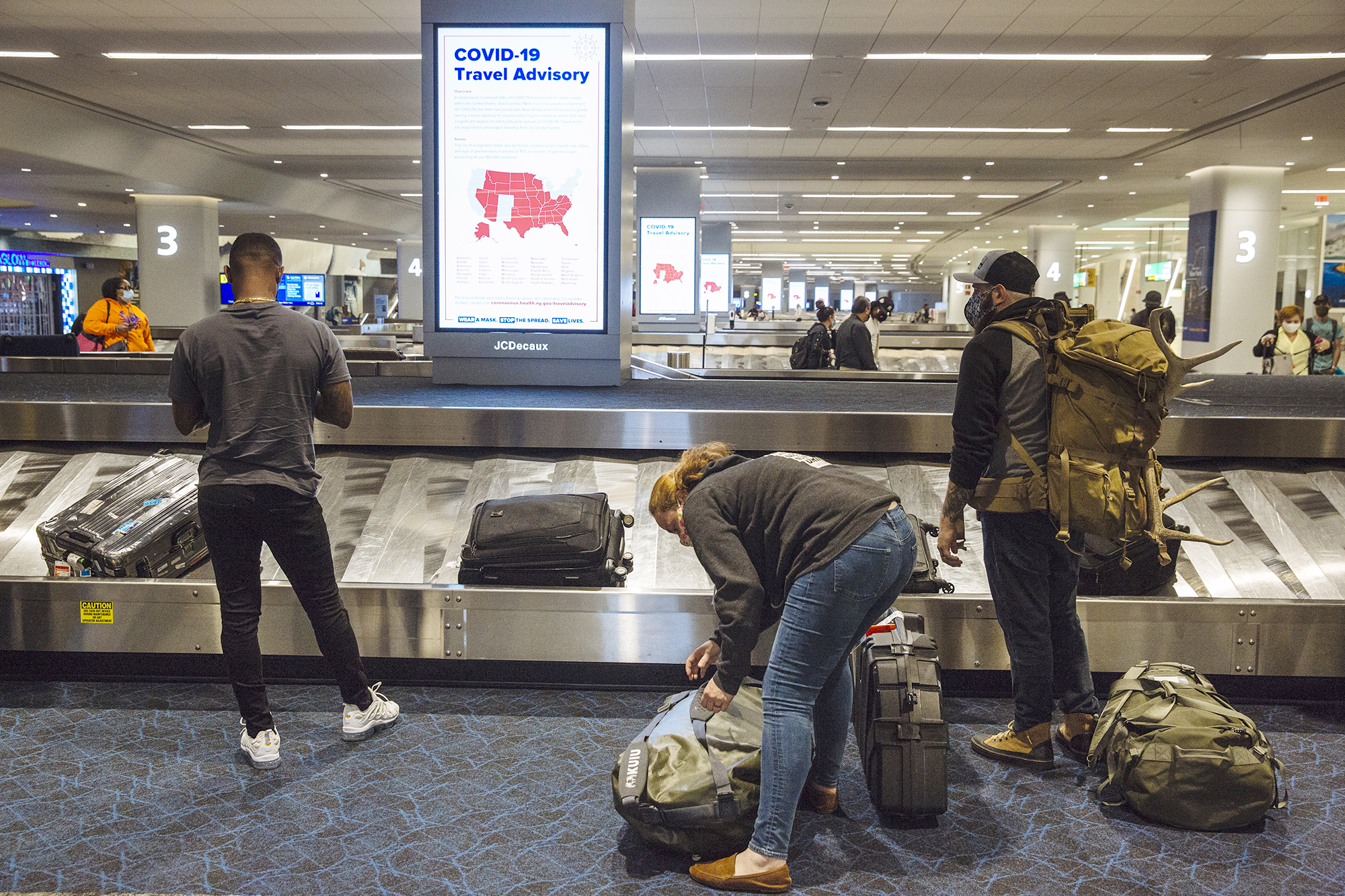 PHOTO: A Covid-19 advisory is displayed on a screen as travelers collect luggage in the baggage claim area of Terminal B at LaGuardia Airport in New York, Sept. 28, 2020.