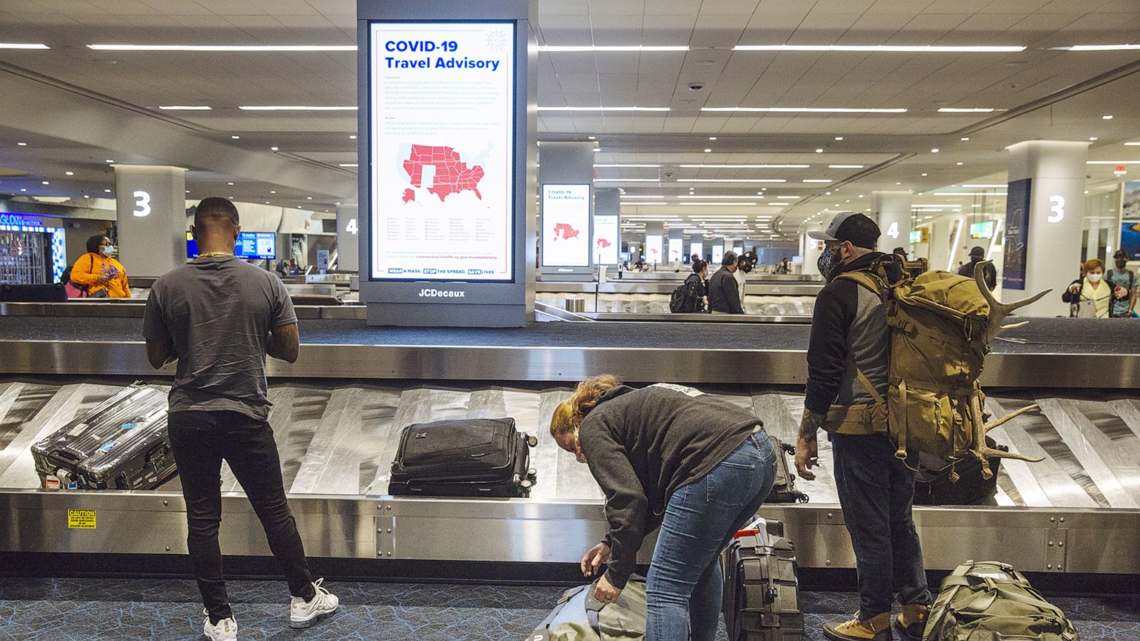 PHOTO: A Covid-19 advisory is displayed on a screen as travelers collect luggage in the baggage claim area of Terminal B at LaGuardia Airport in New York, Sept. 28, 2020.