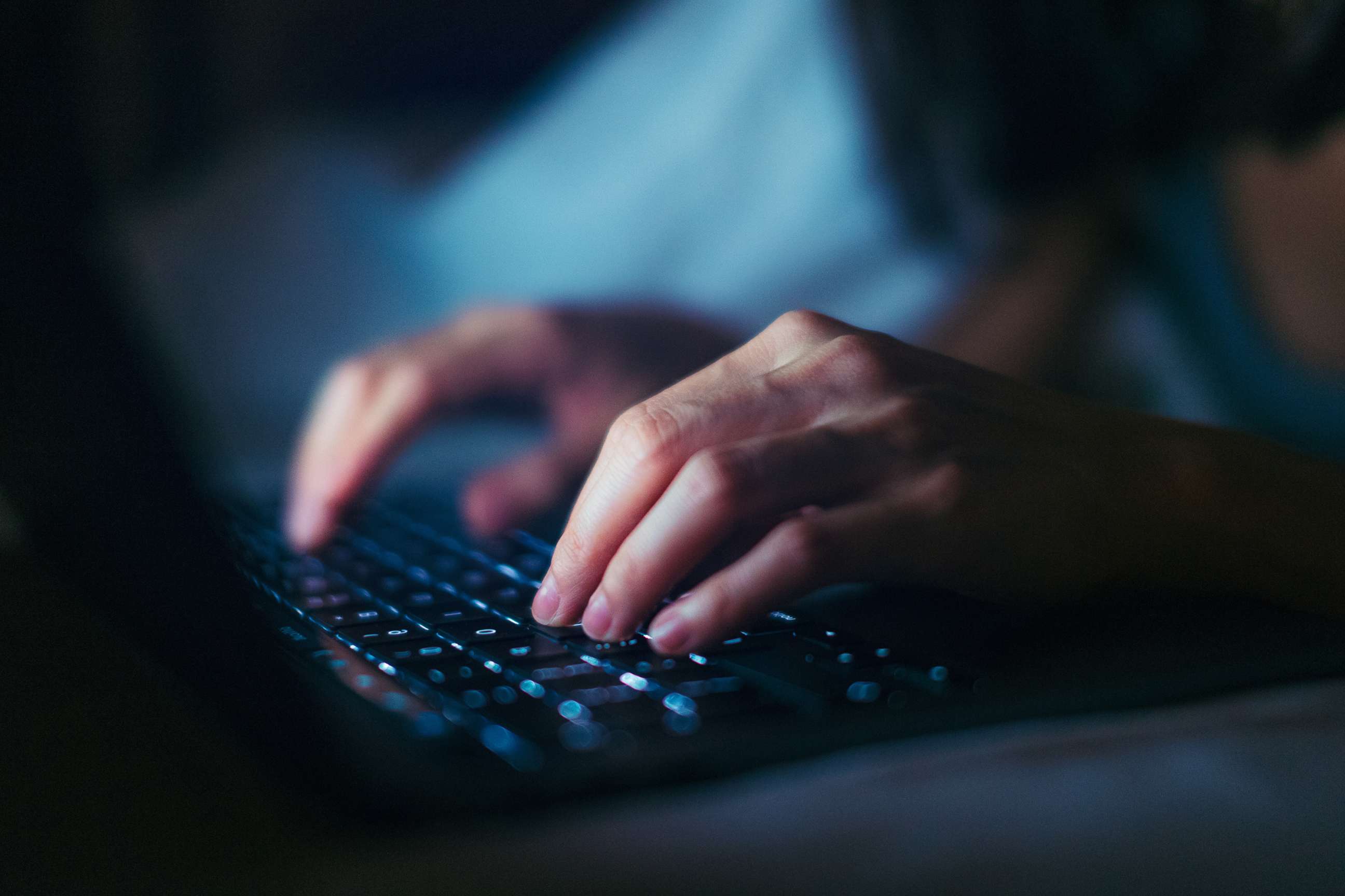 PHOTO: Close-up shot of female hands typing on computer keyboard, lying on bed, working late at home.