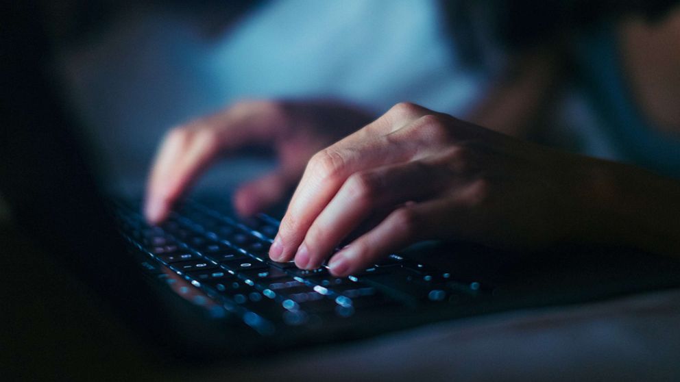 PHOTO: Close-up shot of female hands typing on computer keyboard, lying on bed, working late at home.