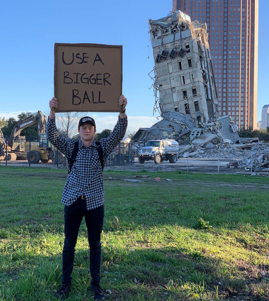 PHOTO: A man holds up a sign with tongue-in-cheek advice for demolition crews at the site of a failed demolition that resulted in a leaning building in Dallas, February 2020.