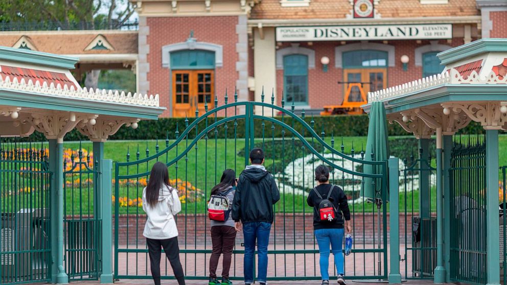 PHOTO: In this file photo taken on March 14, 2020 people stand outside the gates of Disneyland Park on the first day of the closure of Disneyland and Disney California Adventure theme parks as fear of the spread of coronavirus continue, in Anaheim, Calif.