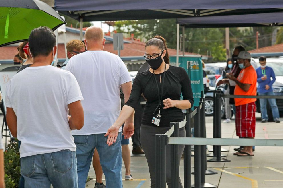 PHOTO: DMV employee Varissa Lopez makes sure people lined up outside the DMV keep a six feet distance from one another, on Aug. 13, 2020 in Westminster, Calif. A sign with information on the Real ID is displayed near the queue.