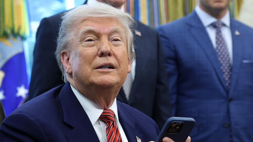 PHOTO: President Donald Trump checks his mobile phone that rang while speaking after signing executive orders in the Oval Office of the White House May 23, 2025 in Washington.