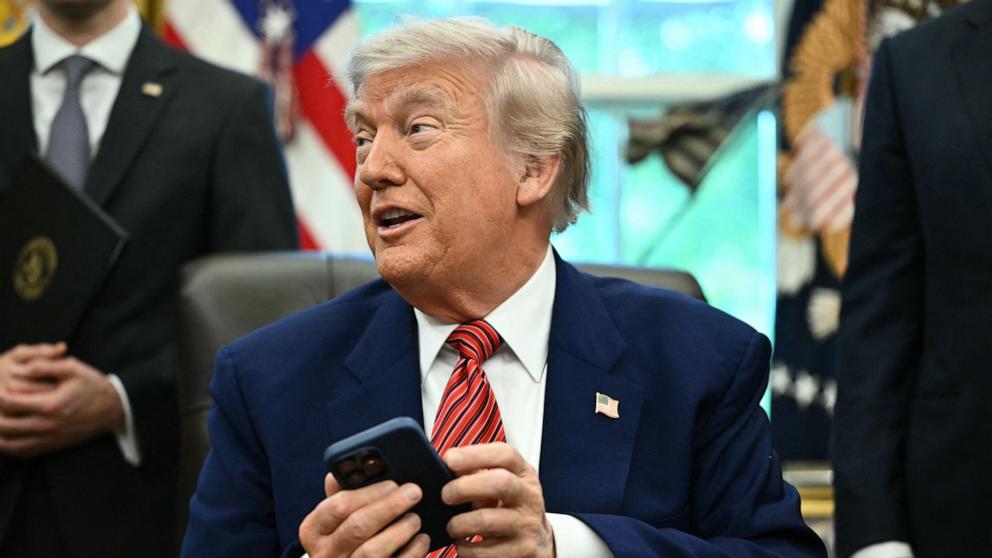 PHOTO: President Donald Trump checks his mobile phone that rang while speaking after signing executive orders in the Oval Office of the White House May 23, 2025 in Washington.