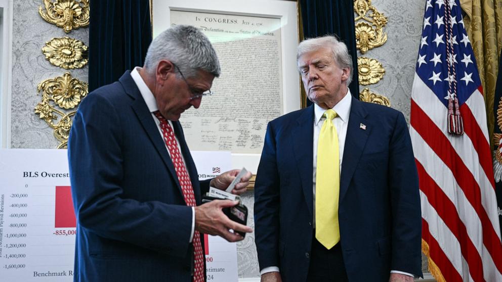 PHOTO: Economist Stephen Moore gives his business card to US President Donald Trump as Trump speaks about the economy in the Oval Office of the White House, Aug. 7, 2025, in Washington.