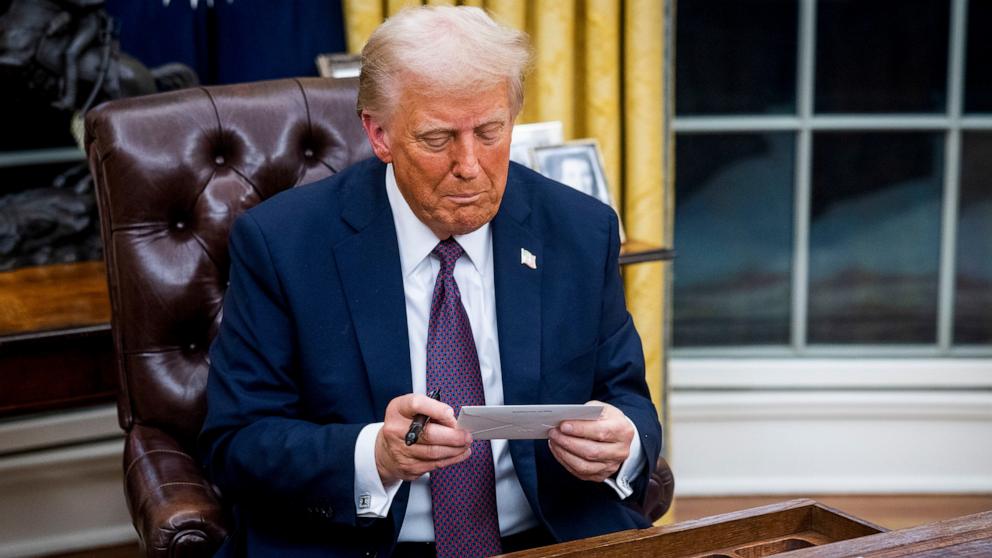 PHOTO: President Donald Trump looks at a letter left for him by former President Joe Biden while signing executive orders in the Oval Office of the White House in Washington, Jan. 20, 2025.