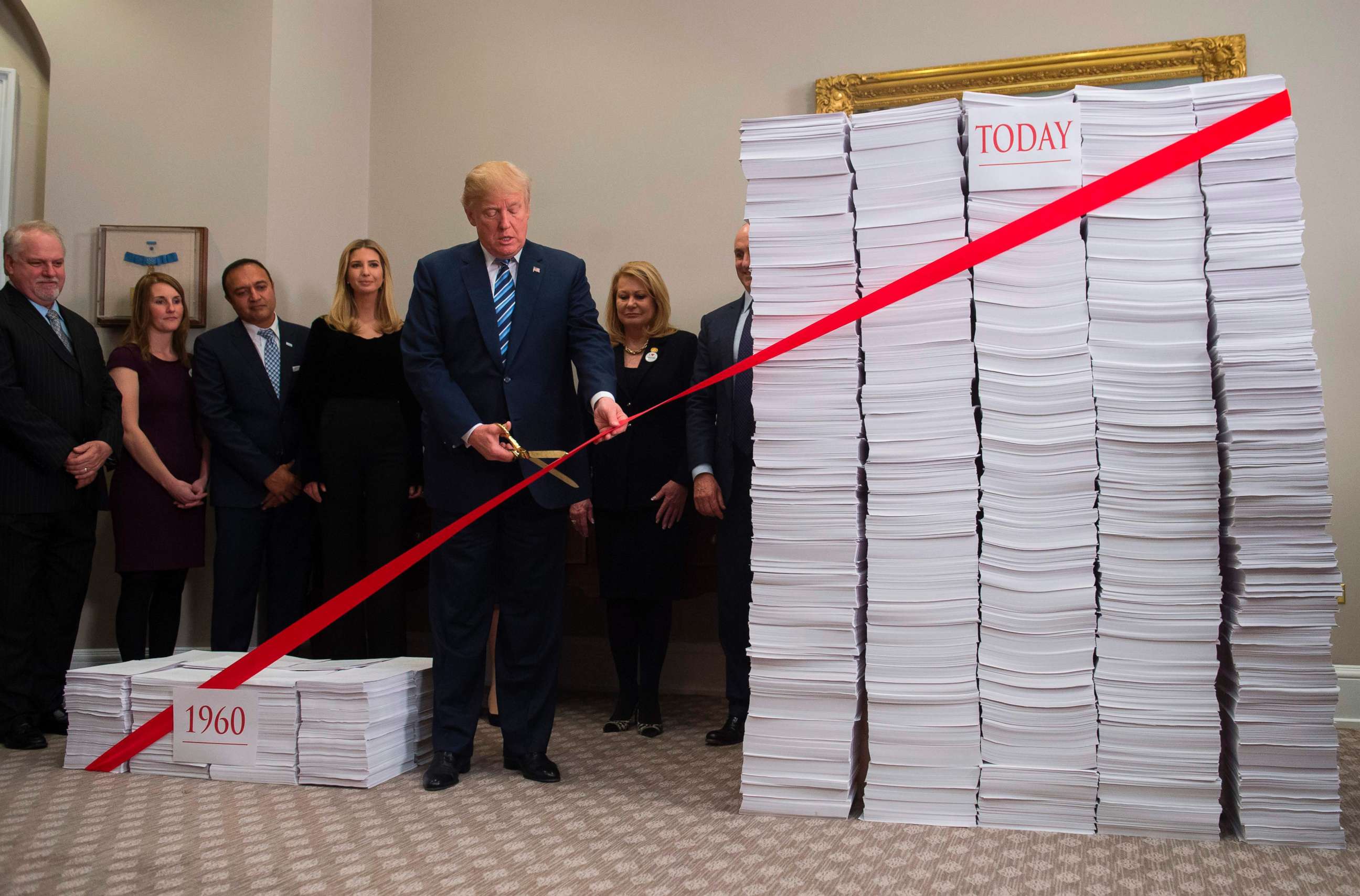 PHOTO: President Donald Trump uses scissors to cut a red tape tied between stacks of papers representing government regulations of the 1960s and today after he spoke about his efforts in deregulation in the White House in Washington, Dec. 14, 2017.