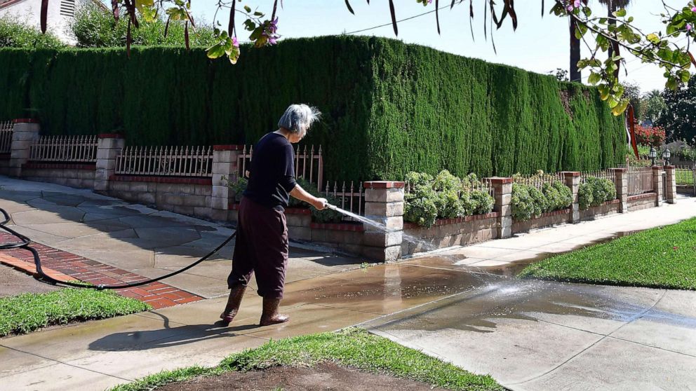PHOTO: A woman waters down her driveway in Monterey Park, Calif., April 27, 2022, a day after Southern California declared a water shortage emergency.