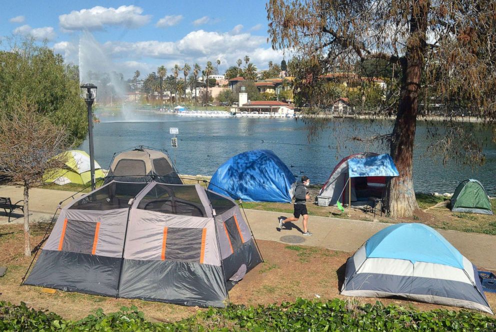 PHOTO: A local resident jogs past a homeless encampment at Echo Park Lake in Los Angeles, March 24, 2021.