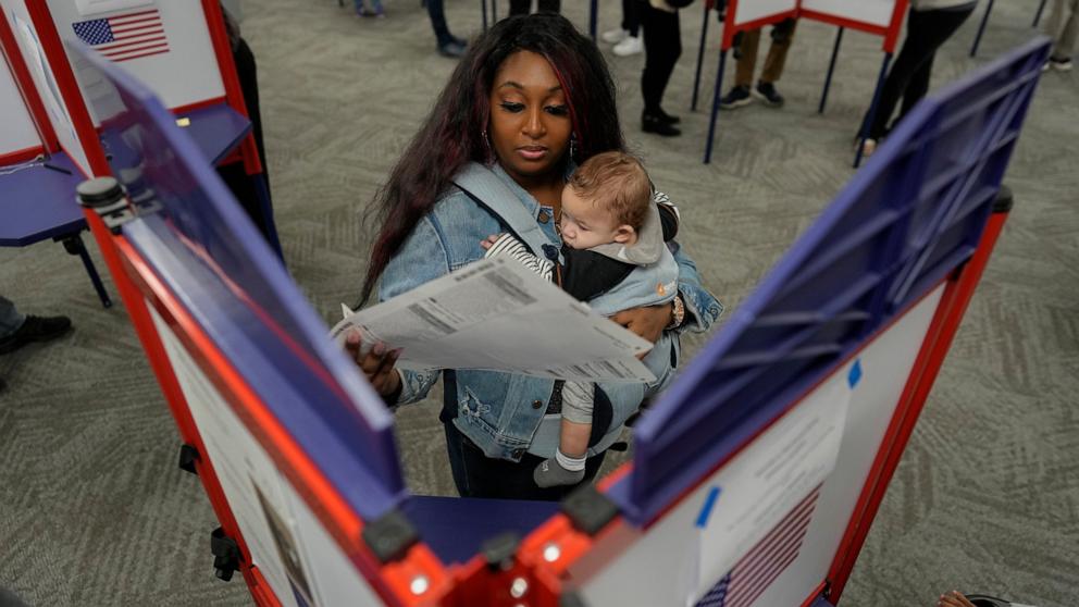 PHOTO: First-time voter Kayria Hildebran holds baby Kayden Hildebran as she fills out her ballot during in-person early voting at Hamilton County Board of Elections, Oct. 31, 2024, in Cincinnati. 