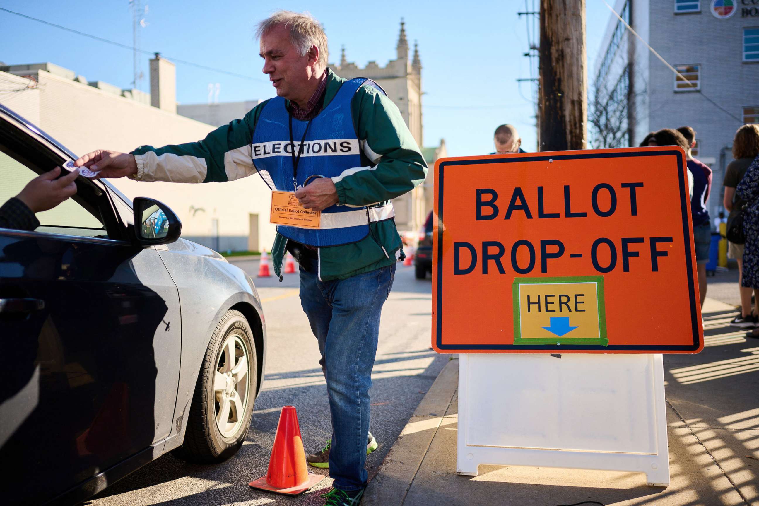 PHOTO: An official ballot collector for the Cuyahoga County Board of Elections gives a voter their "I Voted" sticker after depositing their mail-in ballots into a collection box in Cleveland, Nov. 6, 2022, ahead of the midterm elections. 