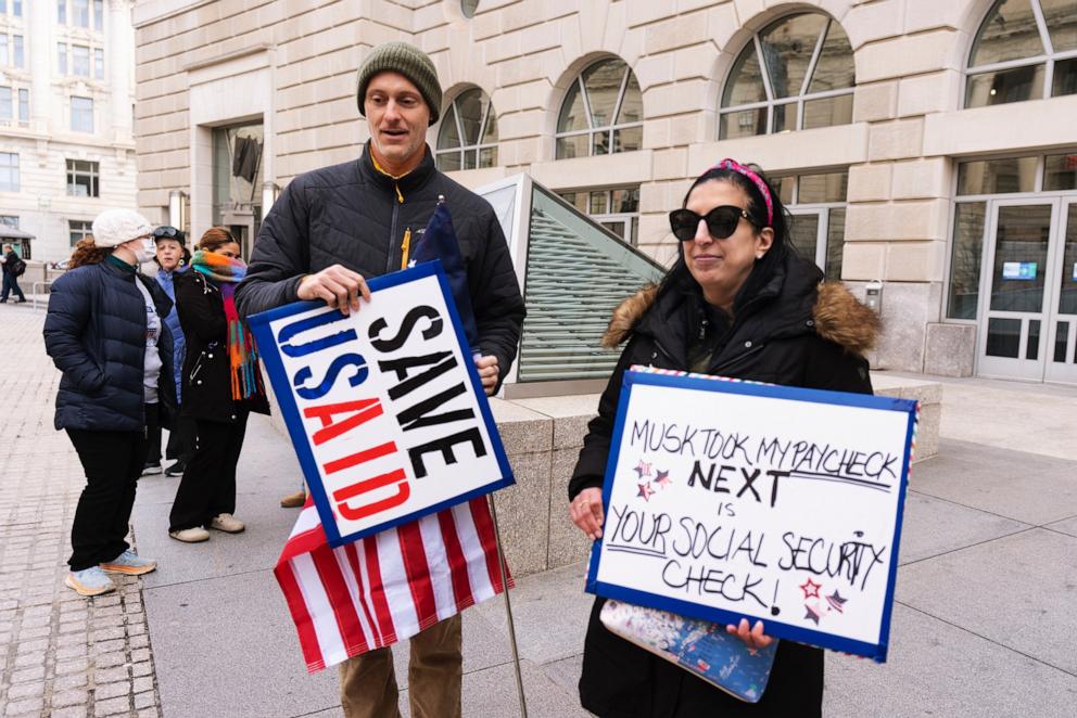 PHOTO: Priya Kathpal, right, and Taylor Williamson, left, who work for a company doing contract work for the U.S. Agency for International Development, or USAID, carry signs outside the USAID headquarters in Washington, Monday, Feb. 10, 2025. 