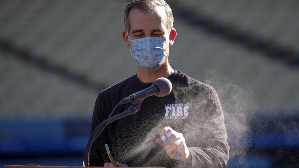 PHOTO: Mayor Eric Garcetti disinfects podium for next speaker at news conference held at the launch of mass COVID-19 vaccination site at Dodger Stadium in Los Angeles, Jan. 15, 2021.