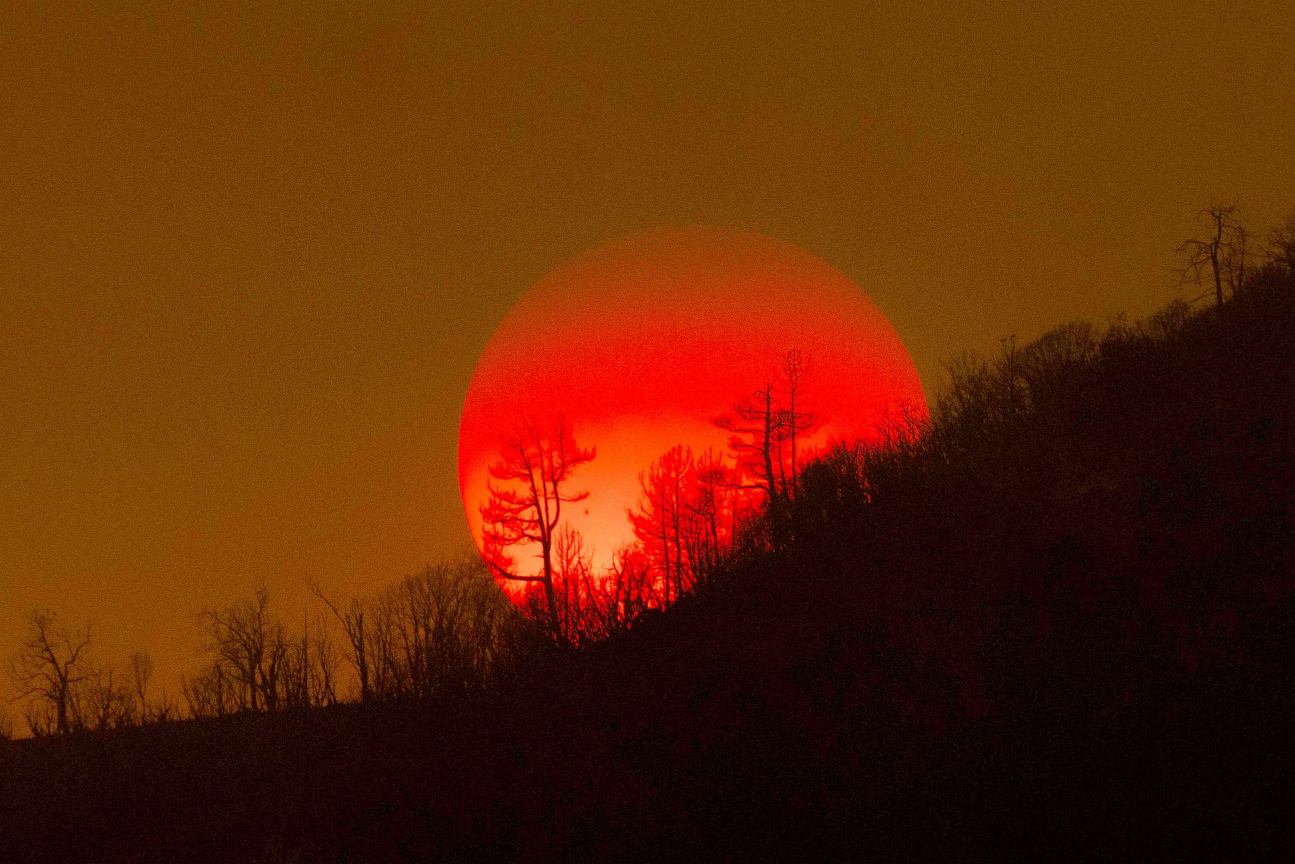 PHOTO: The sun sinks behind a smoky sky and burned forest at the Oak Fire on near Mariposa, Calif.,July 24, 2022. 