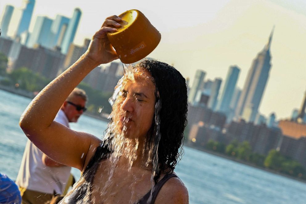 PHOTO: A woman pours water on her face to cool off in a fountain in Domino Park, Brooklyn with the Manhattan skyline in the background as the sun sets during a heat wave in the Brooklyn borough of New York, July 24, 2022.