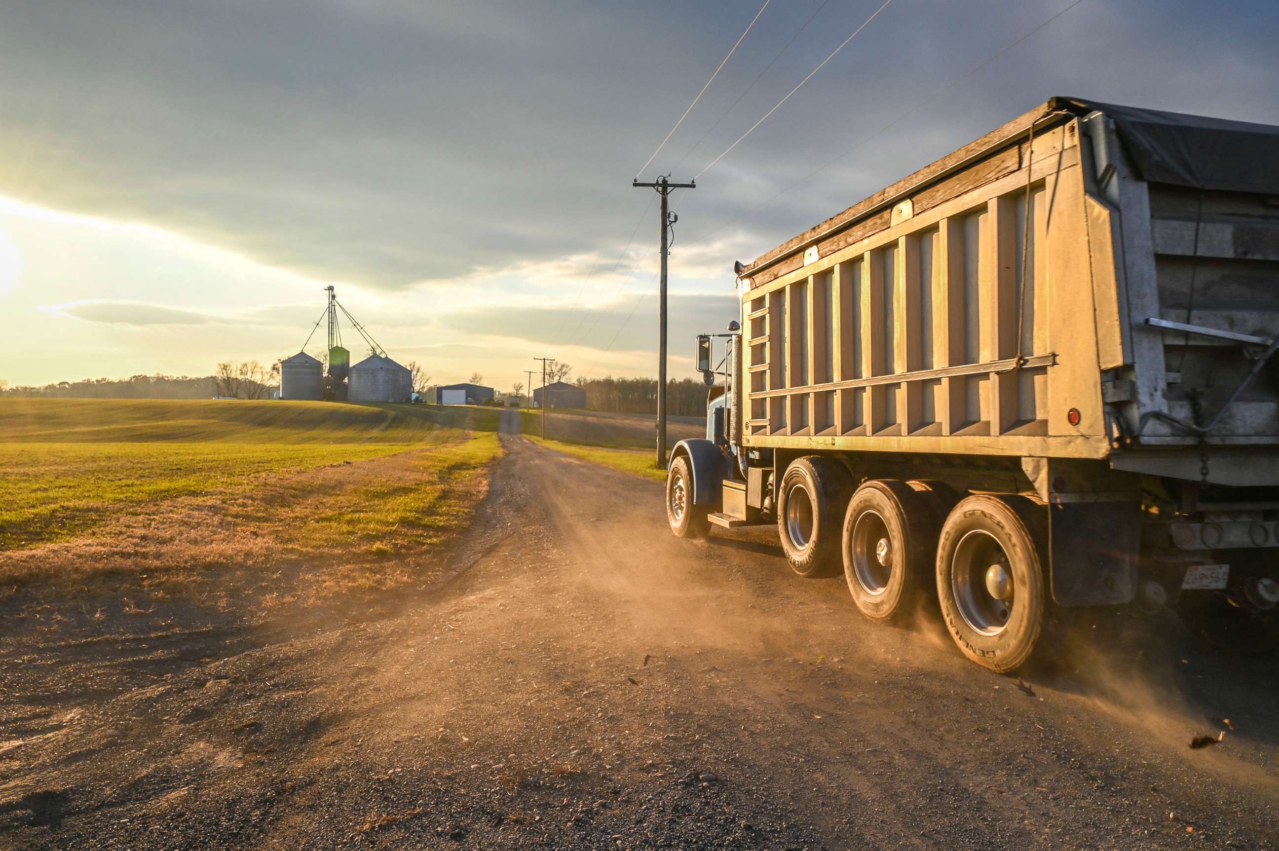 PHOTO: A roll off truck drives down dirt road towards grain silos, Laytonsville Maryland.