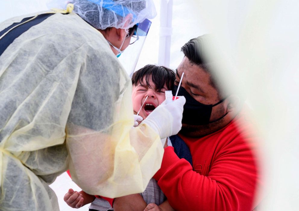 PHOTO: Jose Vatres, right, holds his son Aidin who reacts as nurse practitioner Alexander Panis, left, takes a nasal swab sample to test for COVID-19 at a mobile testing station in a public school parking area in Compton, California, on April 28, 2020.