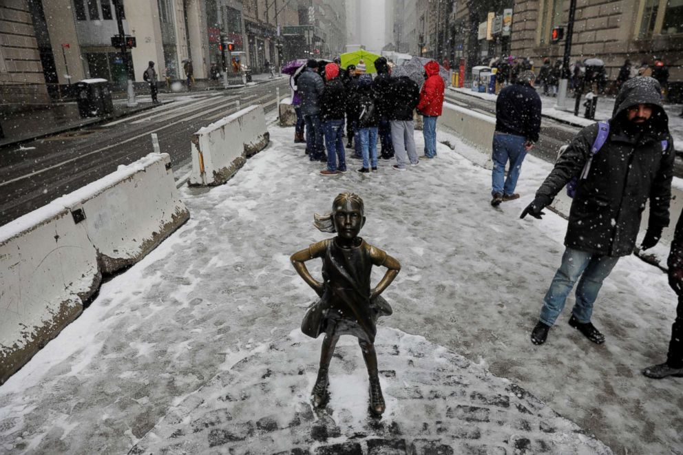 PHOTO: Pedestrians walk past a snow covered "Fearless Girl" sculpture during a late season nor'easter in New York, March 21, 2018.