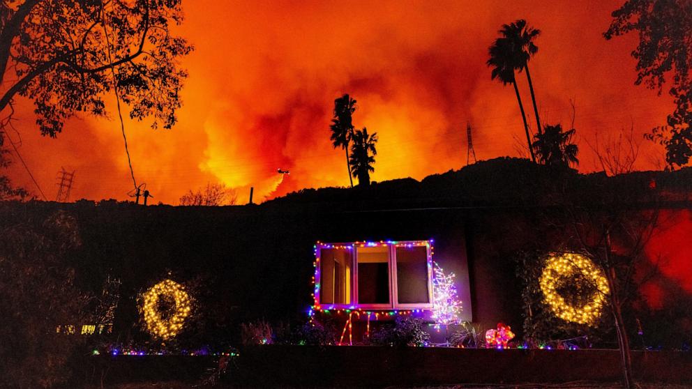 PHOTO: A helicopter drops water on the Palisades Fire behind a home with Christmas lights in Mandeville Canyon, Jan. 10, 2025, in Los Angeles. 