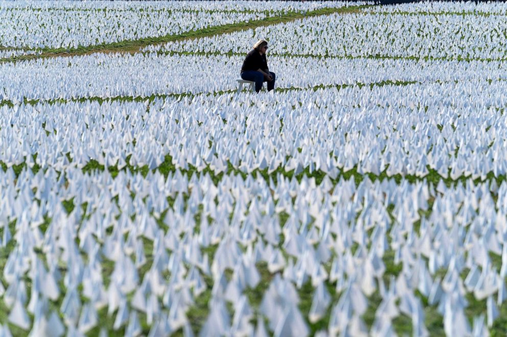 PHOTO: A visitor sits on a bench to look at a temporary art installation made up of white flags to commemorate Americans who have died of COVID-19, on the National Mall, in Washington, D.C., Oct. 2, 2021. 