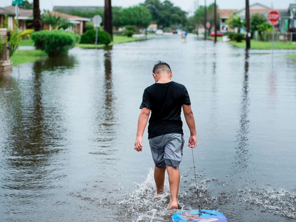 PHOTO: A boy walks with a bodyboard through a flooded street as the effects of Hurricane Harvey are seen Aug. 26, 2017 in Galveston, Texas.