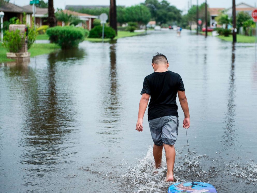PHOTO: A boy walks with a bodyboard through a flooded street as the effects of Hurricane Harvey are seen Aug. 26, 2017 in Galveston, Texas.