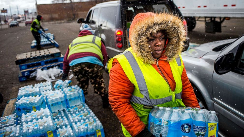 Flint resident Nia Augustine, 26, carries two cases of free bottled water as she fills a vehicle's trunk with eight cases at a water distribution center while cars line up more than 50 deep on Dort Highway, April 6, 2018 in Flint, Mich.