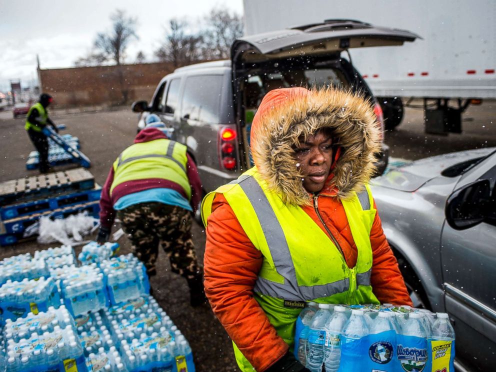 PHOTO: Flint resident Nia Augustine, 26, carries two cases of free bottled water as she fills a vehicles trunk with eight cases at a water distribution center while cars line up more than 50 deep on Dort Highway, April 6, 2018 in Flint, Mich.