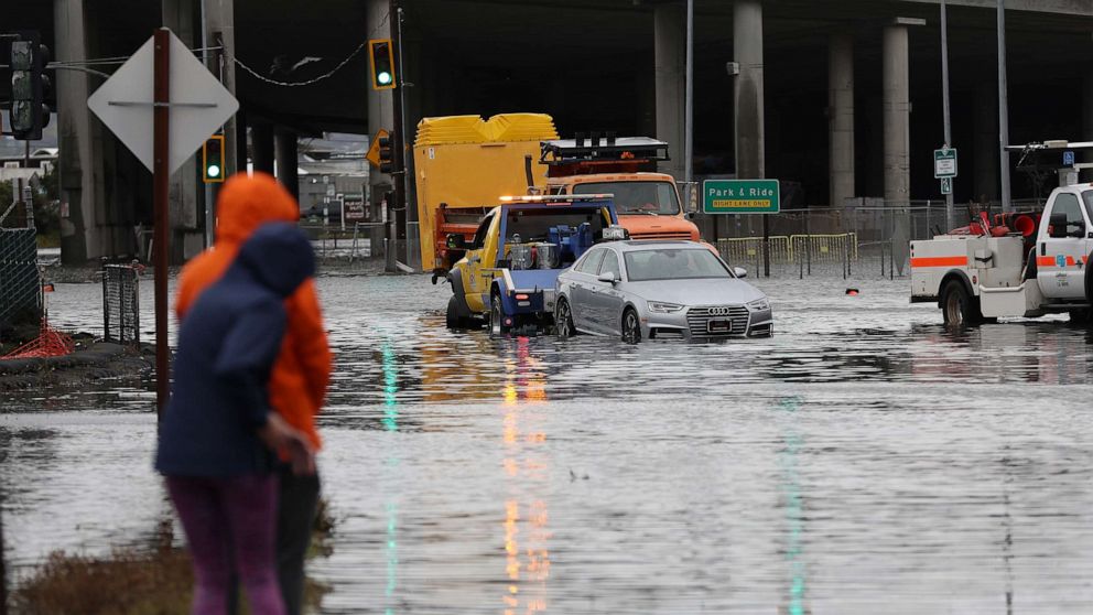 PHOTO: People look on as a tow truck pulls a car out of a flooded intersection, Jan. 4, 2023, in Mill Valley, Calif.