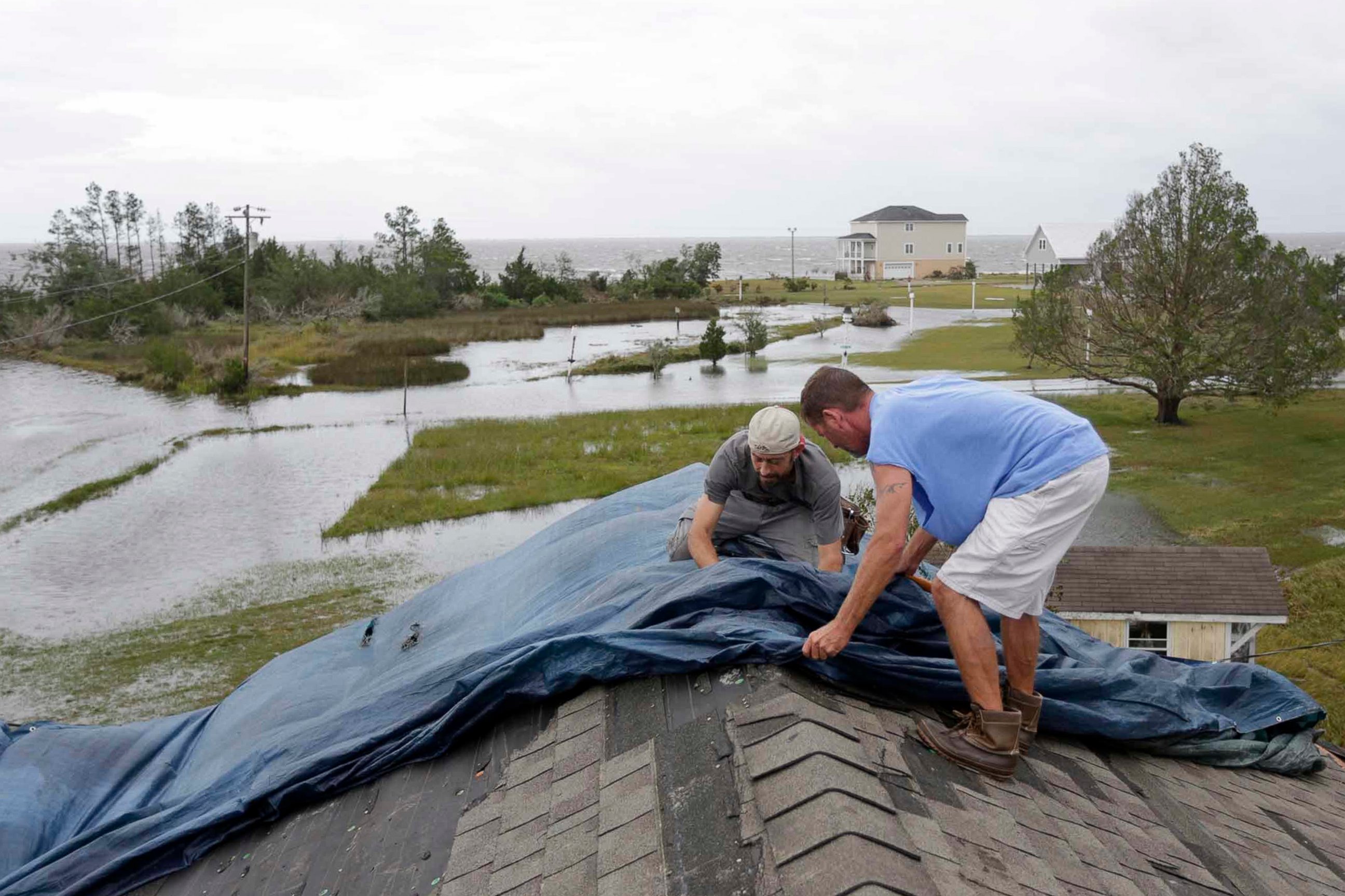 Jeff Pyron, left, and Daniel Lilly cover Lilly's roof after Hurricane Florence hit Davis N.C., Saturday, Sept. 15, 2018. The town had 4 1/2 feet of storm surge. 