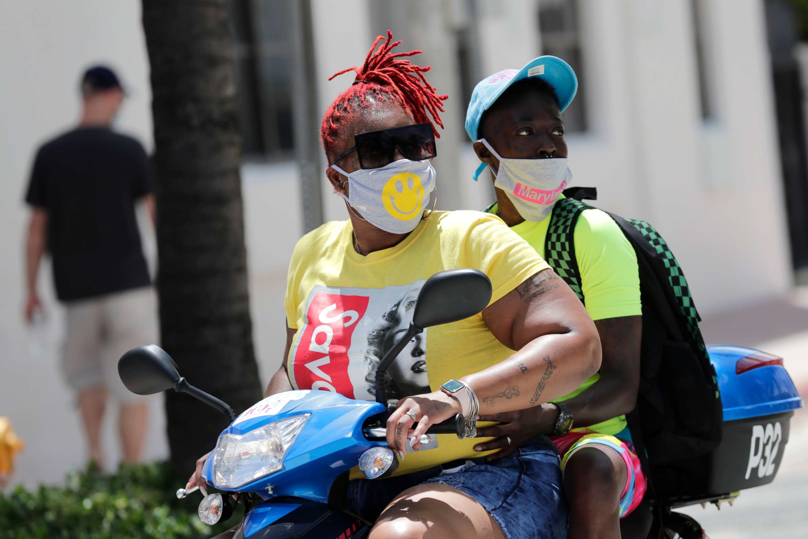 PHOTO: People wearing protective face masks ride a scooter down Ocean Drive during the coronavirus pandemic, July 12, 2020, in Miami Beach, Fla.