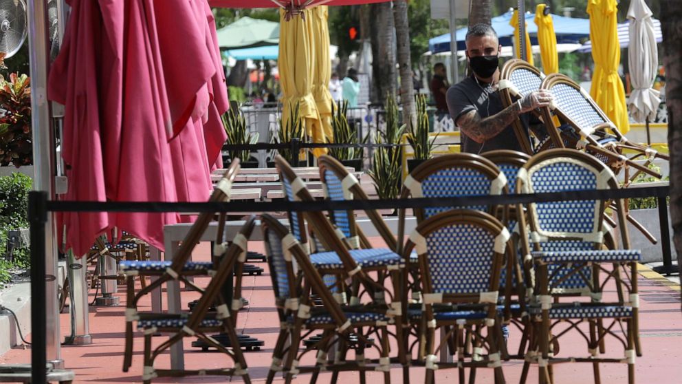 PHOTO: An employee at the Clevelander bar and restaurant on Ocean Drive stacks chairs as they have shut down due to public health concerns caused by COVID-19 during the coronavirus pandemic, July 13, 2020, in Miami Beach, Fla.