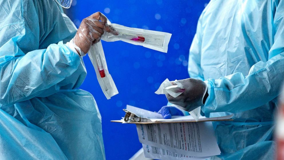 PHOTO: Health care workers prepare a COVID-19 test sample before a person self-administered a test at the COVID-19 drive-thru testing center at Miami-Dade County Auditorium in Miami, July 23, 2020.